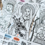Close-up of a folded black-and-white iconography coloring sheet showing saints (St. Francis of Assisi, St. Thérèse of Lisieux) with labeled symbols like halo, crown, crucifix, roses, palm, and open Bible explaining their meanings.