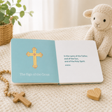 Open board book showing the Sign of the Cross page with a gold cross